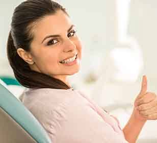 A smiling woman in a dentist’s chair giving a thumbs up