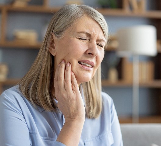 Woman in blue shirt with eyes closed holding right hand to her jaw in pain