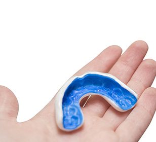 A white and blue mouthguard on the palm of a hand with a white background