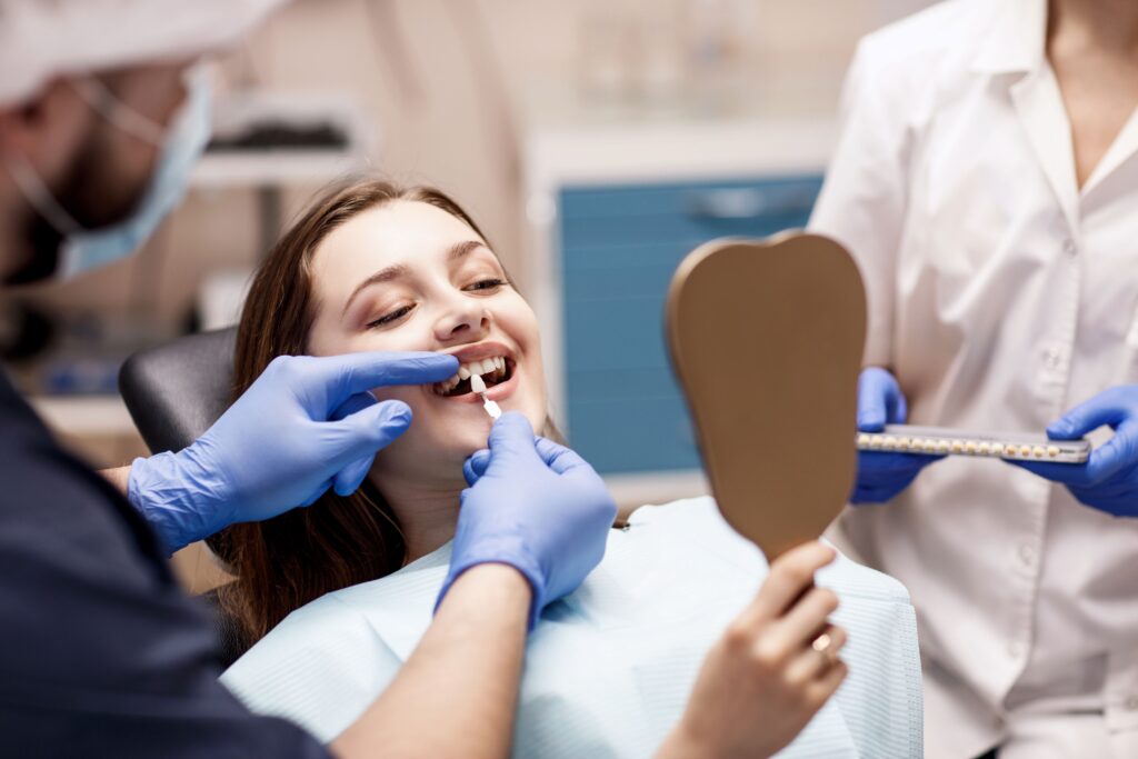 Young woman holding mirror while dentist color-matches her teeth